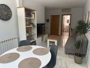 A living room with a dining table, chairs, a bookshelf, a television, and a plant. - Beautiful Apartment in Retiro (Madrid)