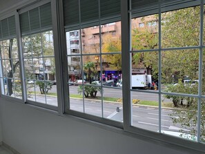 A view from inside a building through large windows, looking out onto a street with parked cars and a building with a neon sign. - Beautiful Apartment in Retiro (Madrid)