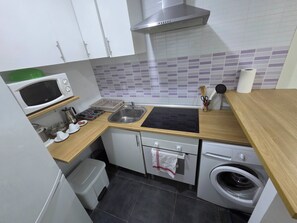 A compact kitchen with a microwave, sink, stove, and washing machine. - Apartment in Fuente del Berro (Madrid)
