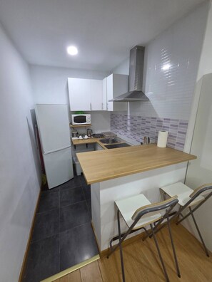 A compact kitchen with a microwave, sink, and a small dining area with two chairs. - Apartment in Fuente del Berro (Madrid)