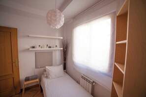 A bedroom with a bed, a bedside table, a radiator, a window with blinds, a hanging light fixture, and a wooden door. - Flat with parking in the center of Las Rozas (Las Rozas)