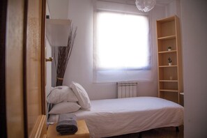 A bedroom with a single bed, a radiator, a window with sheer curtains, a bedside table with a lamp, and a wooden bookshelf. - Flat with parking in the center of Las Rozas (Las Rozas)