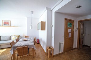 Un comedor con una mesa lista para cuatro, un sofá, un taburete pequeño y un extintor.