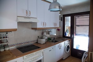 A compact kitchen with white cabinets, a built-in oven, a washing machine, and a window with blinds. - Flat with parking in the center of Las Rozas (Las Rozas)