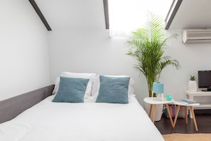 Ein modernes Hotelzimmer mit einem Bett, einem kleinen Beistelltisch, einer Zimmerpflanze und einem Fernseher.