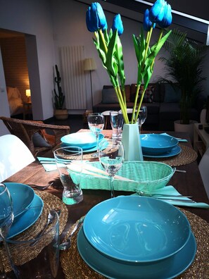 Ein Esstisch ist mit blauen Tellern, klaren Gläsern und einer Vase mit blauen Blumen gedeckt.