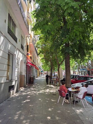 A sidewalk café with outdoor seating, a tree-lined street, and buildings with balconies. - Apartment in Barrio de las Letras (Madrid)