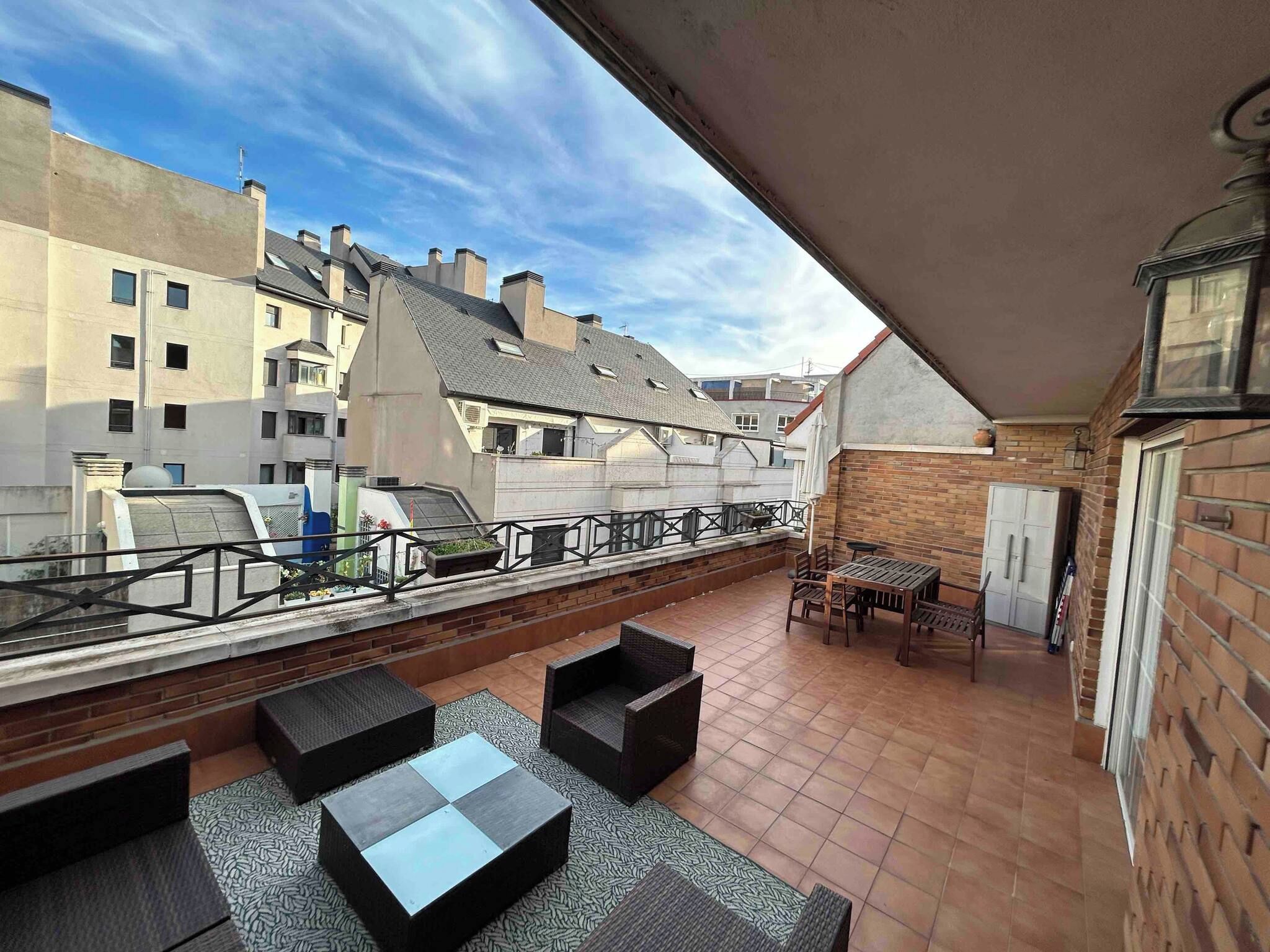 Une terrasse sur le toit, aménagée avec du mobilier d’extérieur, offrant une vue sur les bâtiments environnants et un ciel dégagé.