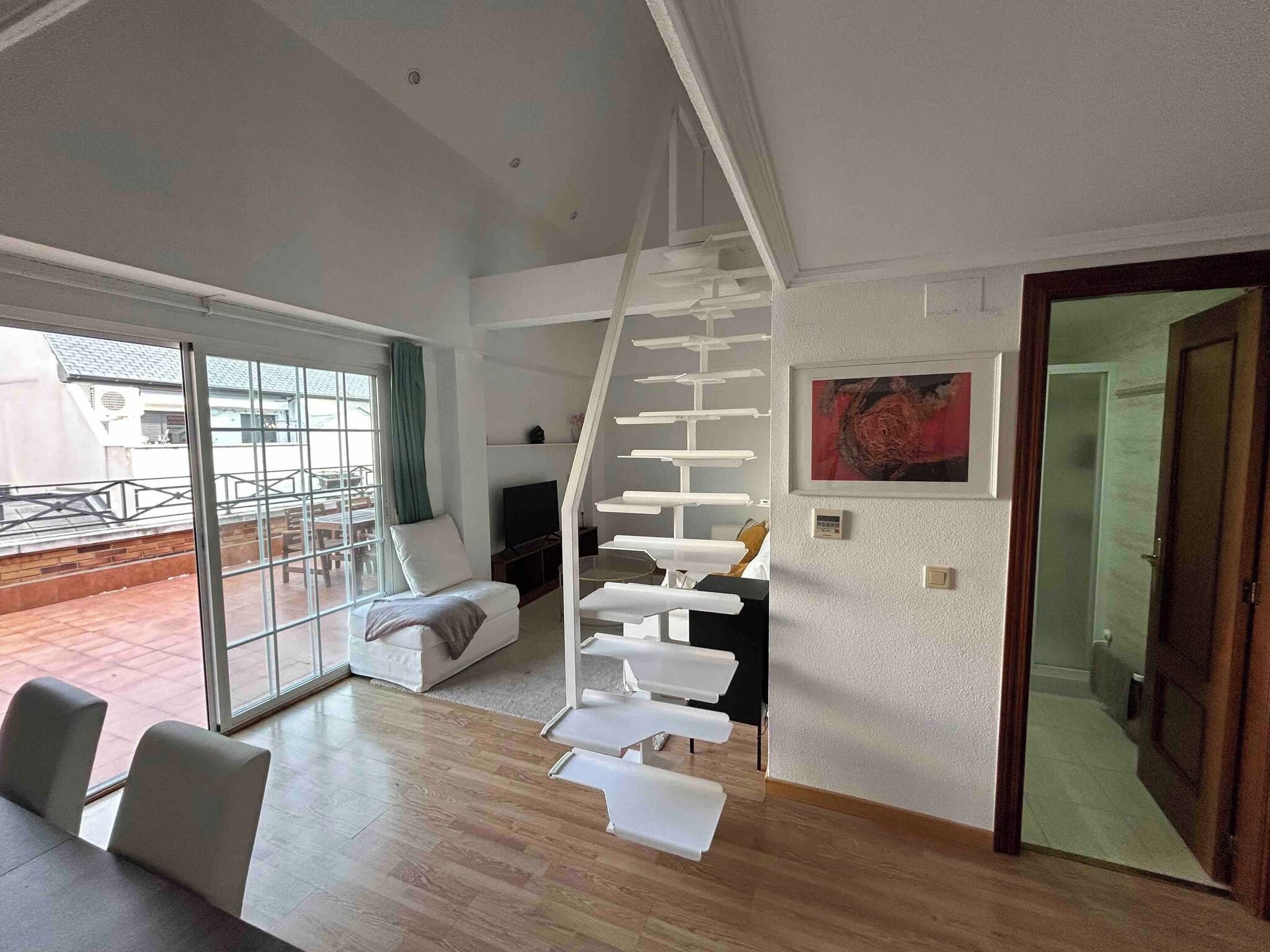 Un salon moderne avec un escalier blanc, un canapé, un coin repas et une grande fenêtre.