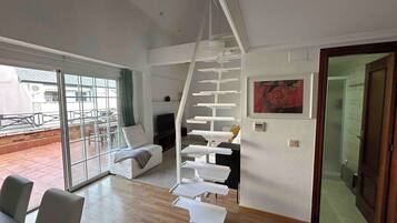 Un salon moderne avec un escalier blanc, un canapé, un coin repas et une grande fenêtre.