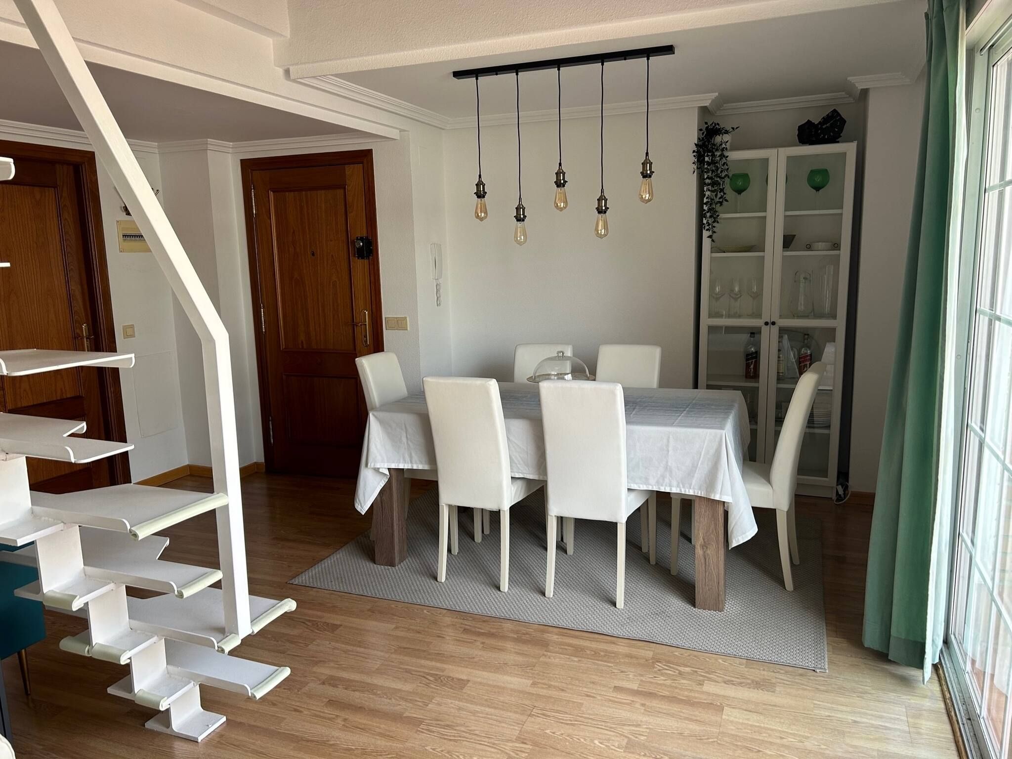 A dining area with a table, chairs, and a hanging light fixture.