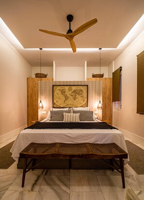 Ein Schlafzimmer mit einem Bett, einem Deckenventilator, einer Weltkarte an der Wand und einer Bank.