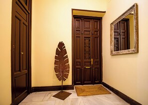 Un pasillo con una puerta de madera, una gran escultura con forma de hoja y un espejo en la pared.