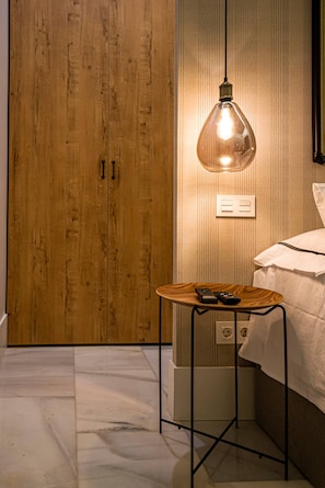 A hotel room with a wooden wardrobe, a hanging light fixture, a small wooden table with a remote control, and a bed with a white cover. - 100 m² of luxury in the heart of the Salamanca neighborhood. (Madrid)