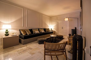 A modern living room with a sofa, a coffee table, and a chair. There is a lamp on a side table, and a door with a radiator next to it. - 100 m² of luxury in the heart of the Salamanca neighborhood. (Madrid)