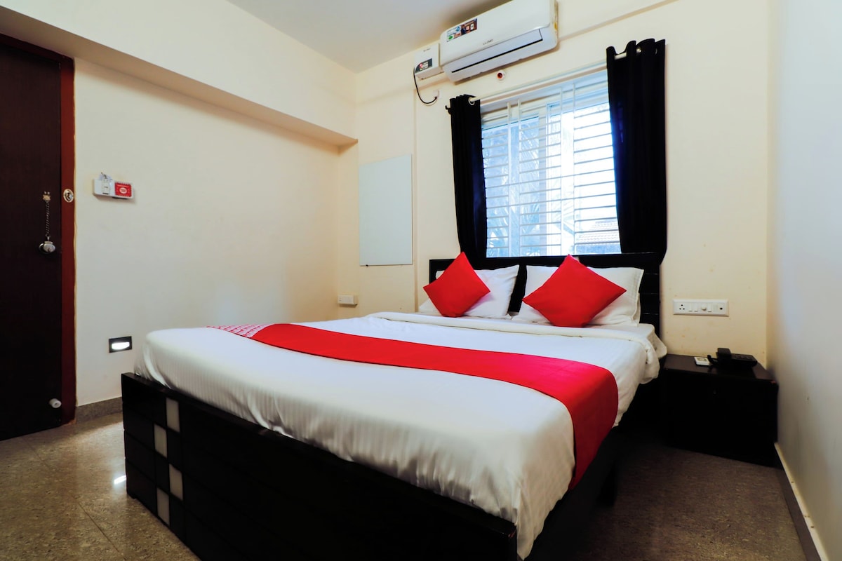 Habitació d'hotel amb un llit, una tauleta de nit, un aparell d'aire condicionat, una finestra amb cortines i una porta.