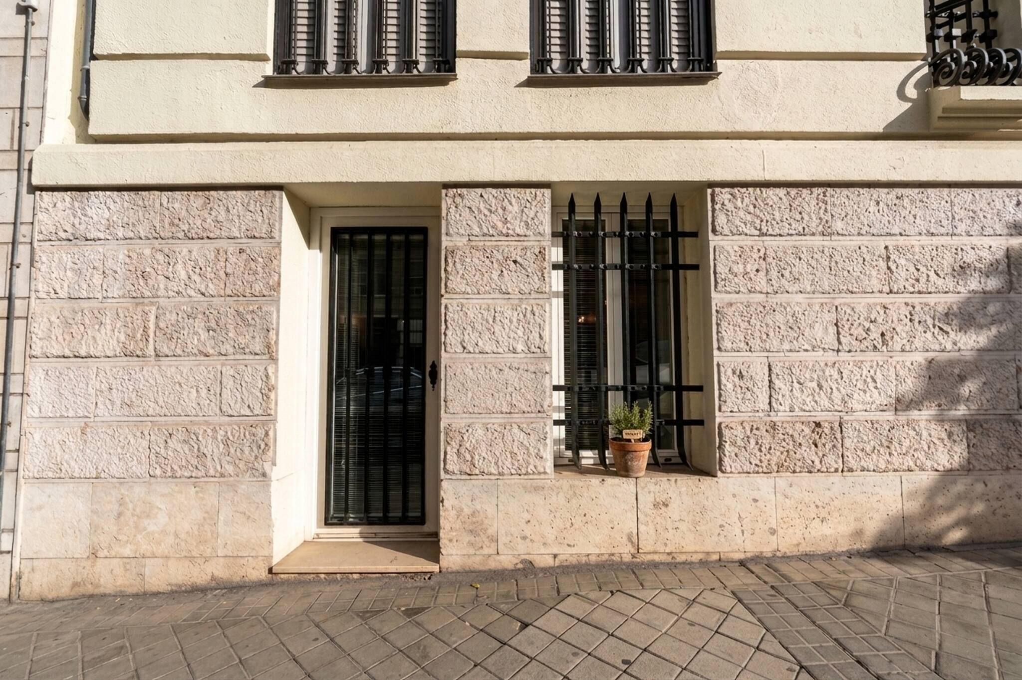 Fachada de un edificio con revestimiento de piedra, una puerta y dos ventanas con barrotes.