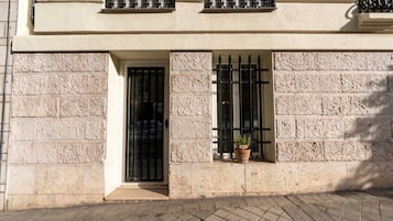 Fachada de un edificio con revestimiento de piedra, una puerta y dos ventanas con barrotes.