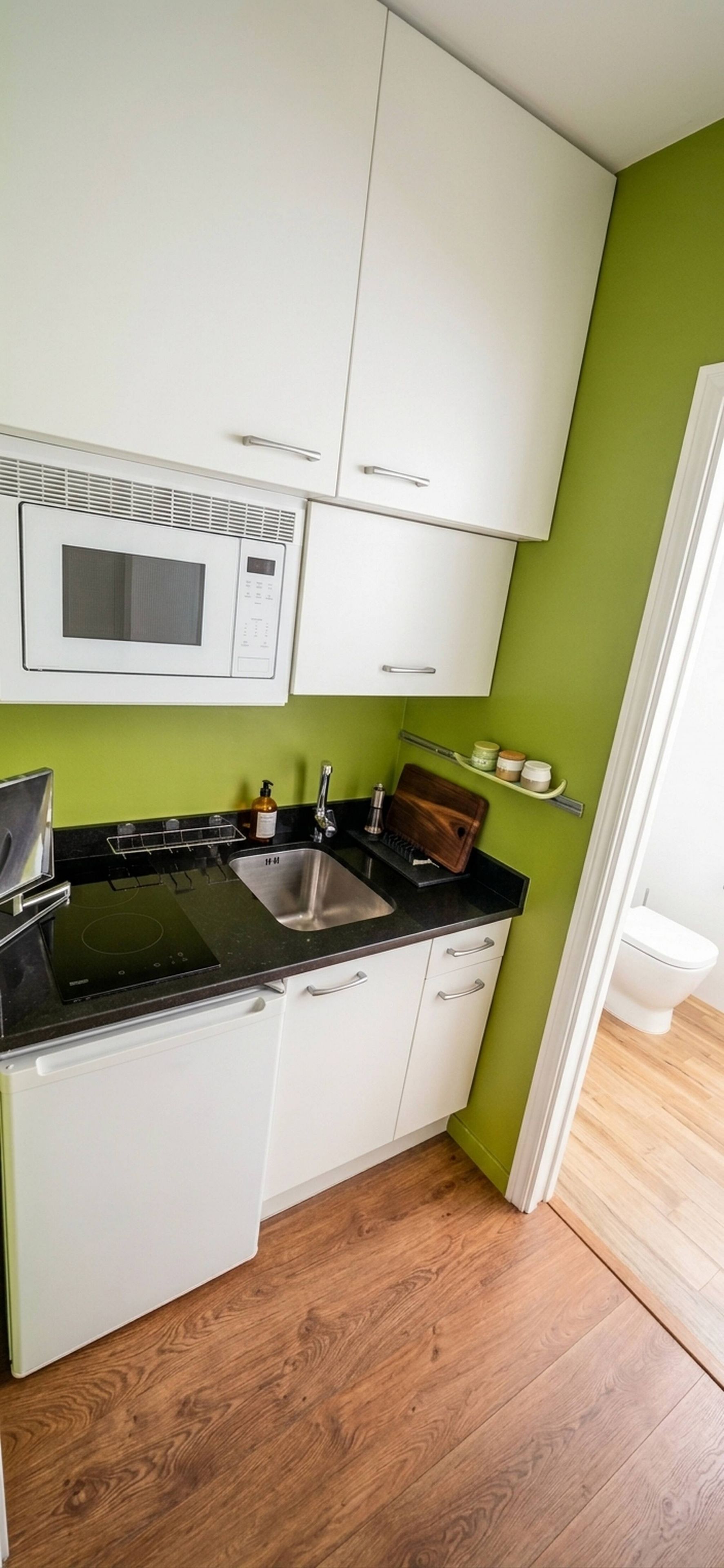 Una cocina compacta con armarios blancos, encimera negra, pileta de acero inoxidable y microondas.