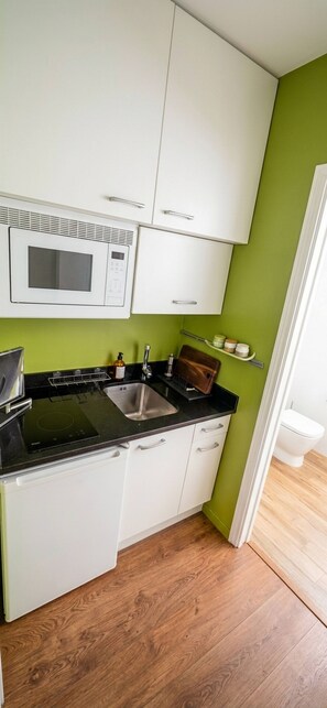A compact kitchen with white cabinets, a black countertop, a stainless steel sink, and a microwave. - Charming Loft in the Heart of the Salamanca Neighborhood (Madrid)