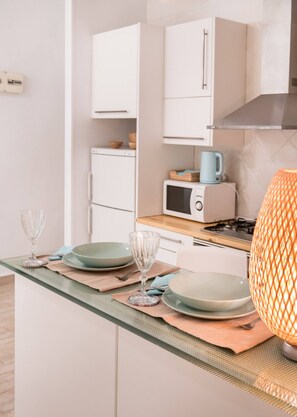 A kitchen with white cabinets, a microwave, a stove, and a table set with plates and a glass. - Cosy and warm at Madrid's heart. A real finding. (Madrid)