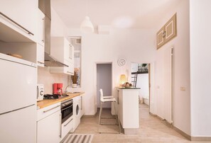 A compact kitchen with white cabinetry, a stove, a coffee maker, and a small dining area with a chair. - Cosy and warm at Madrid's heart. A real finding. (Madrid)