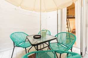 A small outdoor seating area with a table and chairs, a watering can, and a door leading to an interior space. - Cosy and warm at Madrid's heart. A real finding. (Madrid)