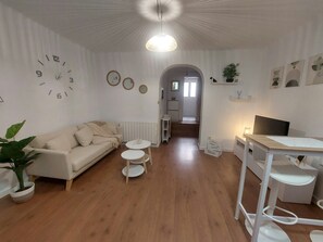 A living room with a sofa, coffee table, and TV stand. There is a kitchen in the background. - Urban Serenity Apartment (Madrid)