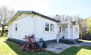 A single-story house with a covered porch, a front yard with potted plants, and a clear sky. - The Little River Cottage - by the Meander River Deloraine (Deloraine)