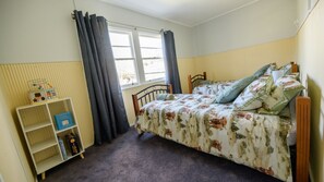 A bedroom with a bed, a window with curtains, a bedside table, and a shelf with books. - The Little River Cottage - by the Meander River Deloraine (Deloraine)