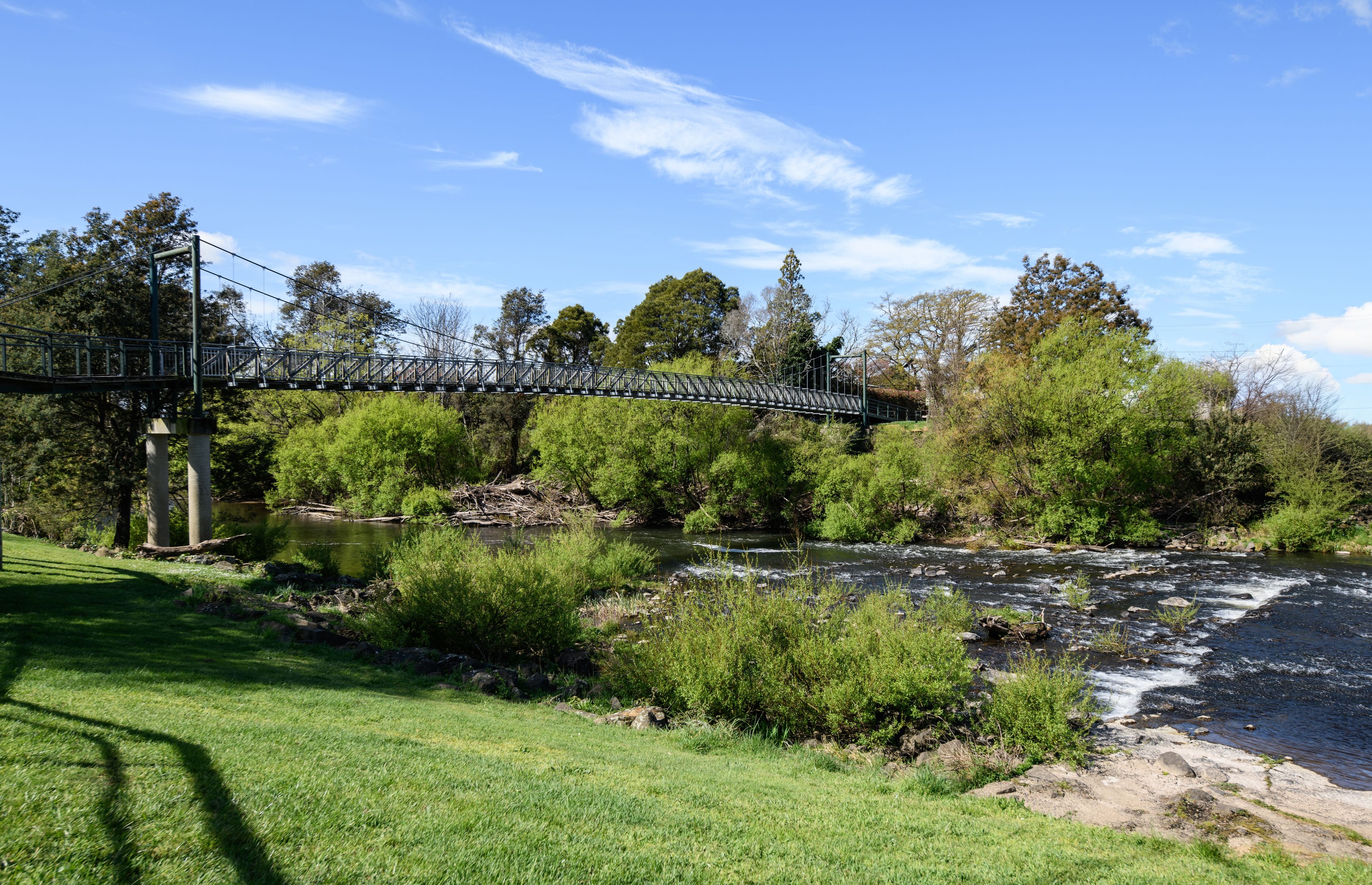 A suspension bridge over a river with surrounding greenery and trees.