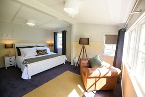 A bedroom with a large bed, bedside lamps, a floor lamp, a leather sofa, and a window with curtains.
