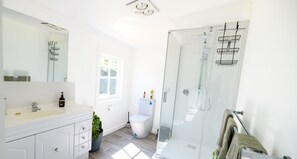 A modern bathroom with a white vanity, a glass shower enclosure, and a window.