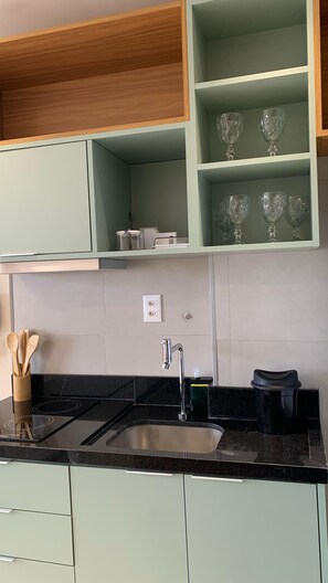 A kitchen with a black countertop, a stainless steel sink, a coffee maker, and a set of wooden utensils. - Beau Studio, with a view of the sea in the iconic Rio Vermelho neighborhood (Salvador)
