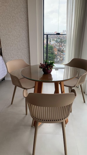 A modern dining area with a round glass table, two chairs, and a potted plant. - Beau Studio, with a view of the sea in the iconic Rio Vermelho neighborhood (Salvador)