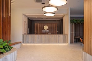 Ett välkomstområde med en receptionsdisk i trä, en skylt som hänger på väggen och en sittgrupp med en växt.