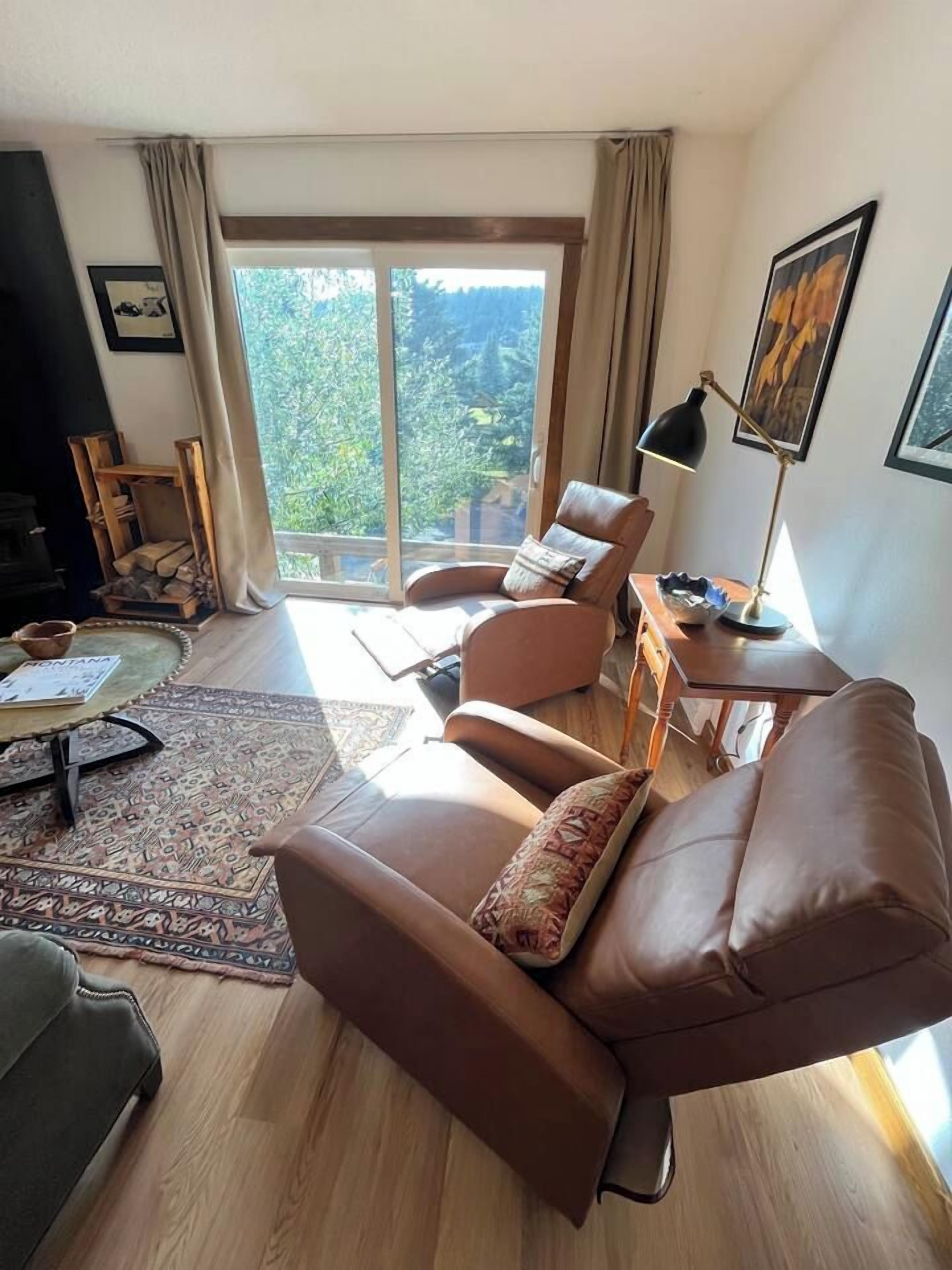 A living room with a brown leather sofa, a round coffee table, and a view of a mountainous landscape through a large window.