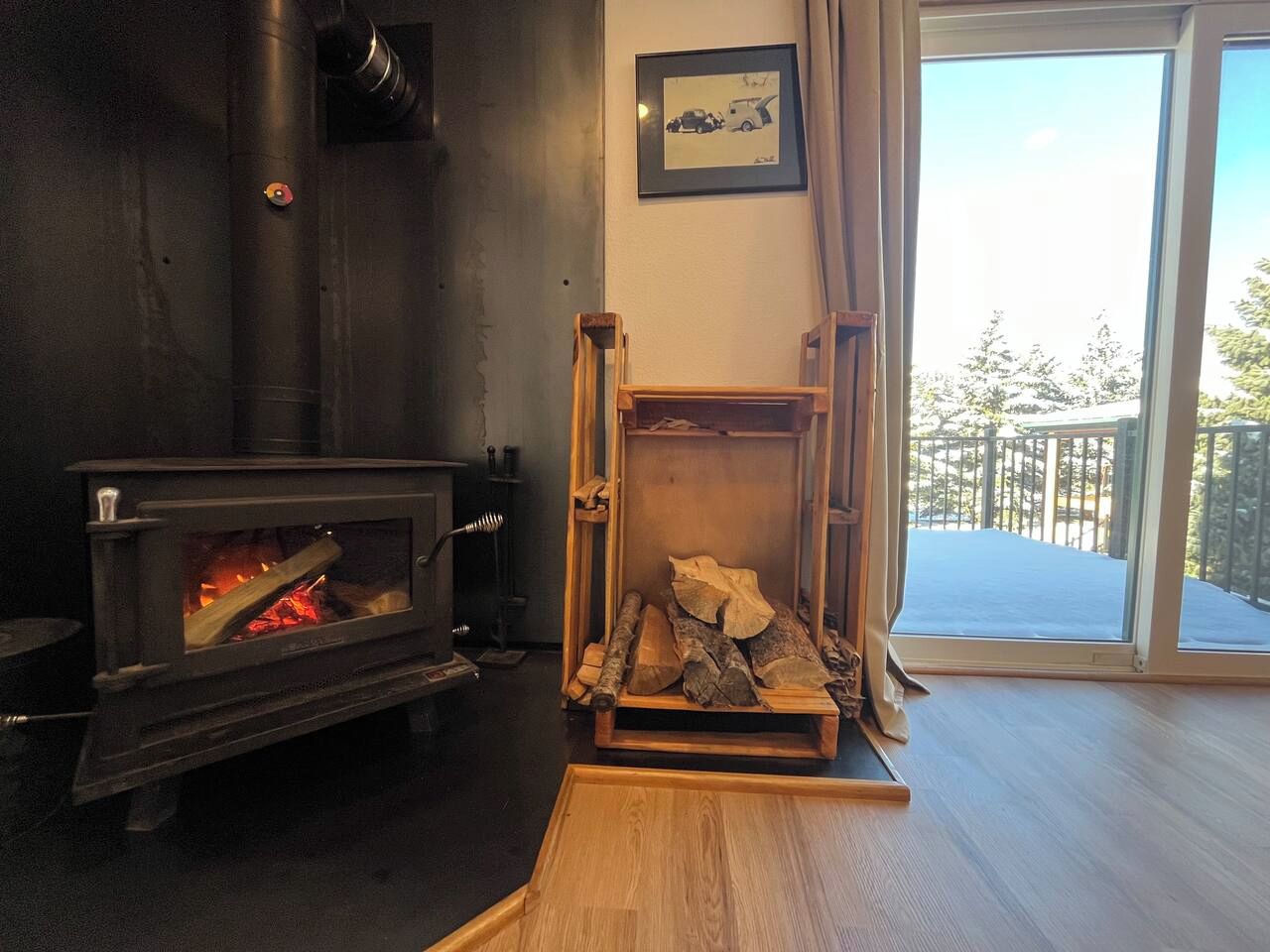 Una habitación con estufa de leña, chimenea y ventana con vistas a un balcón.