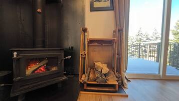 Una habitación con estufa de leña, chimenea y ventana con vistas a un balcón.