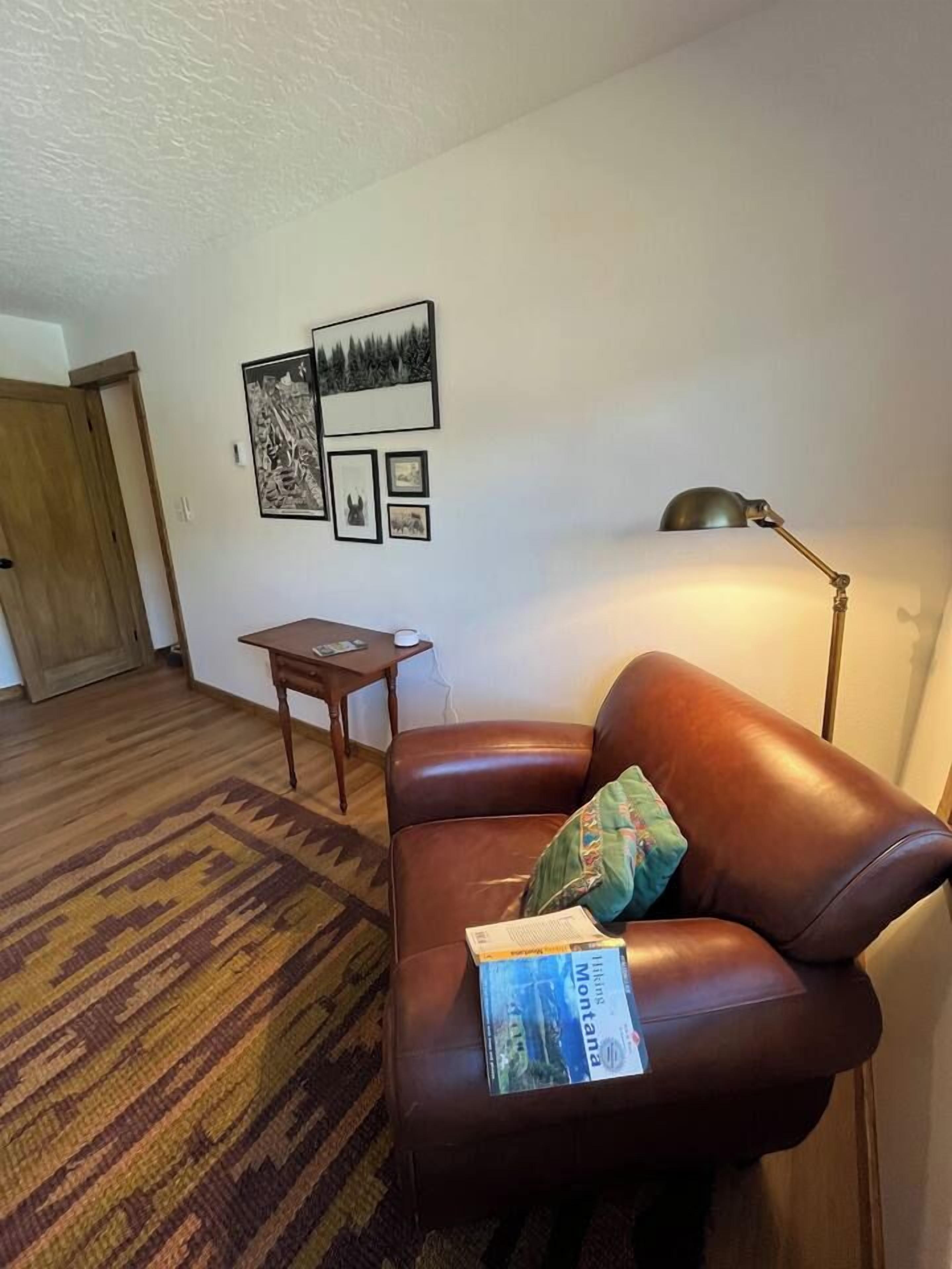 Une pièce avec un canapé en cuir marron, une petite table en bois, un tapis à motifs et des œuvres d’art accrochées au mur.