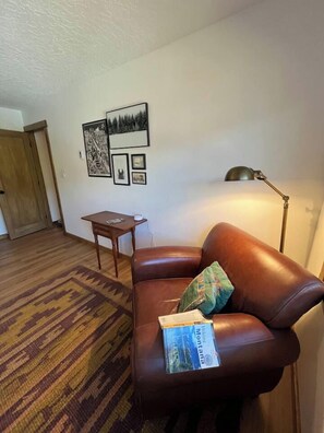 Une pièce avec un canapé en cuir marron, une petite table en bois, un tapis à motifs et des œuvres d’art accrochées au mur.