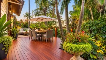 Une terrasse en bois avec une table et des chaises, entourée d’une végétation tropicale luxuriante et de palmiers.