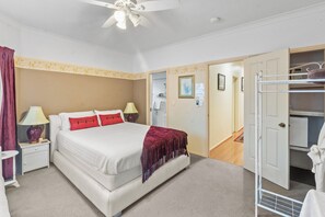 A bedroom with a bed, nightstands, a ceiling fan, a wardrobe, and a bathroom visible through an open door.