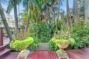 A wooden deck with two large planters, surrounded by various tropical plants and trees.