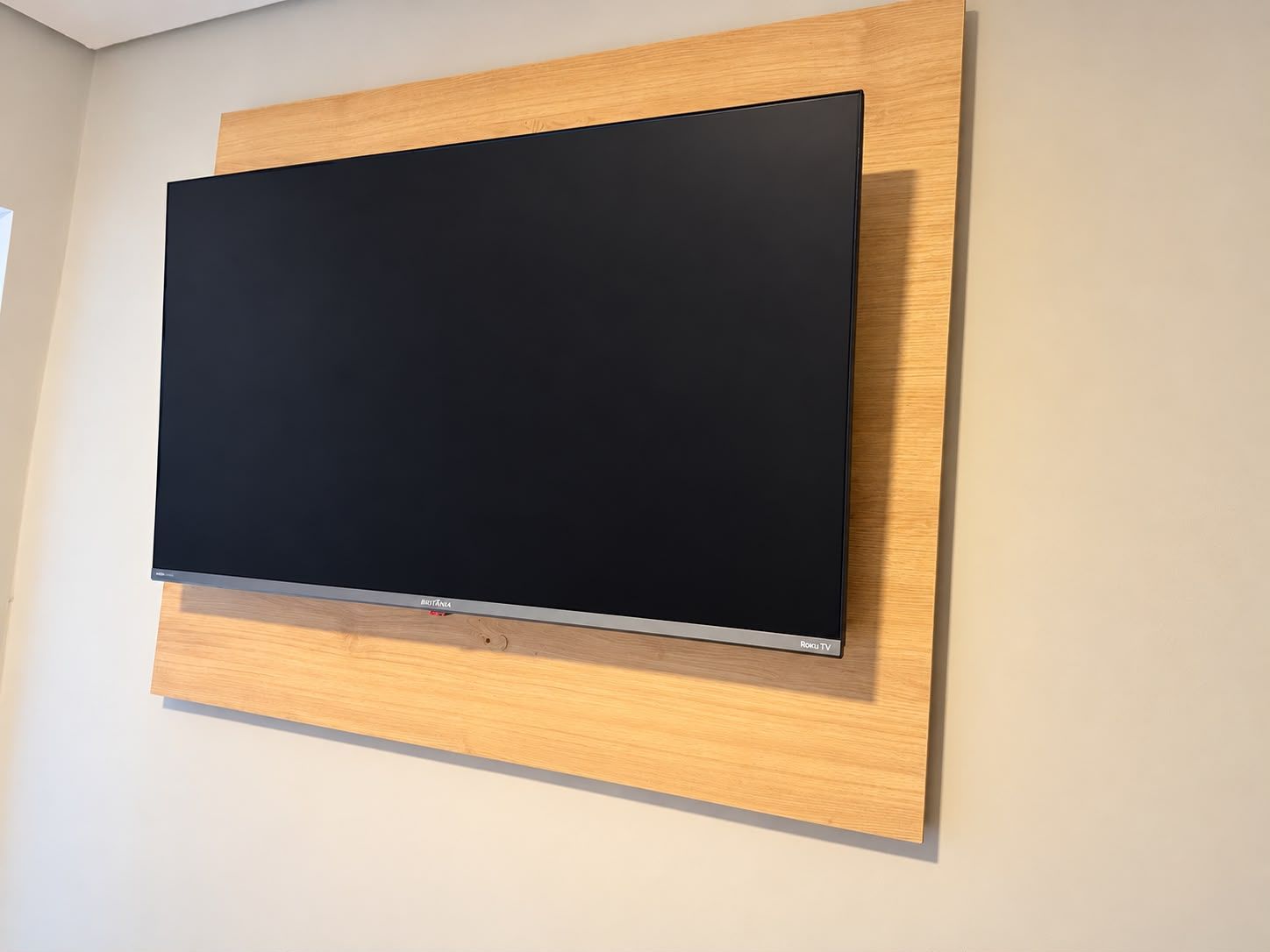 A flat-screen TV mounted on a wooden panel against a wall.