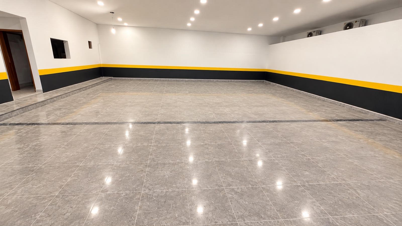 A spacious indoor area with a tiled floor and a yellow and black stripe running along the lower wall.