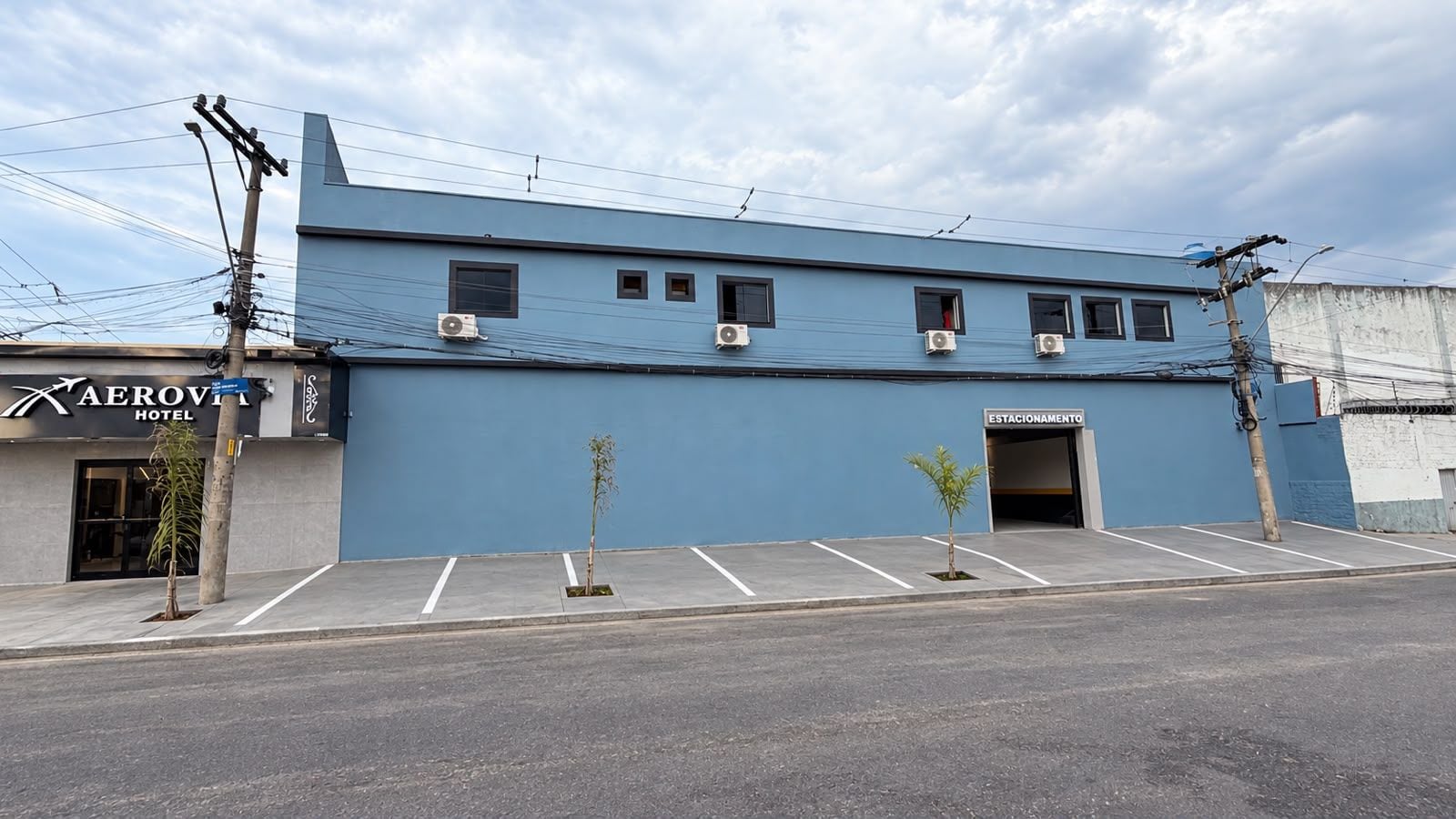 A hotel building with a blue facade, multiple air conditioning units, a parking area, and a sign indicating a stationing area.