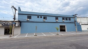 Edificio de hotel con fachada azul, múltiples unidades de aire acondicionado, zona de estacionamiento e indicación de área de estacionamiento.