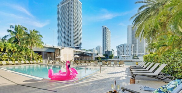 Ein Poolbereich mit Liegestühlen, einem Flamingo-Schwimmpflege und hoch aufragenden Gebäuden im Hintergrund.