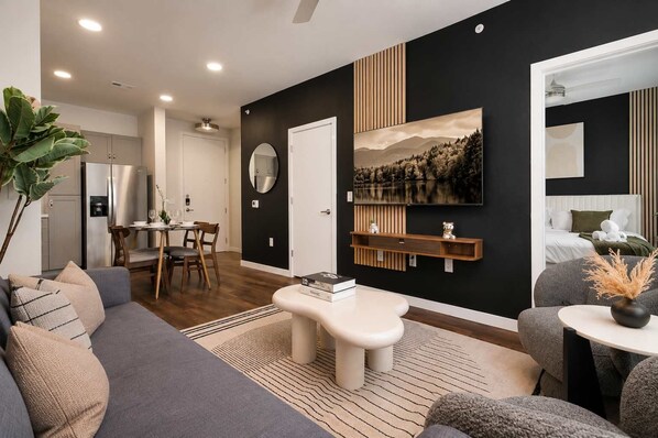 A modern living room with a sofa, coffee table, and a dining area with chairs and a table. - Modern Downtown Retreat with Pool and Gym (San Antonio)